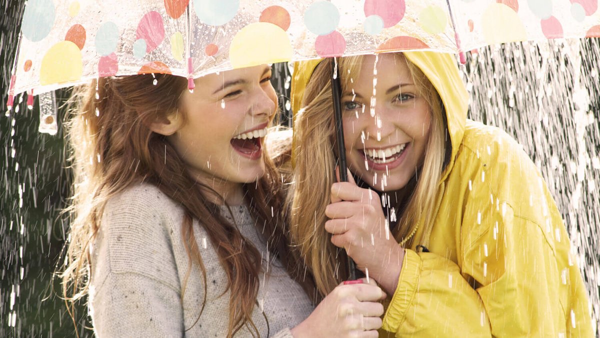 Дві молоді жінки сміються під парасолькою