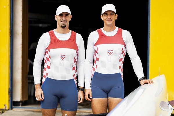 Двоє спортсменів стоять поруч із човном для веслування та посміхаються.