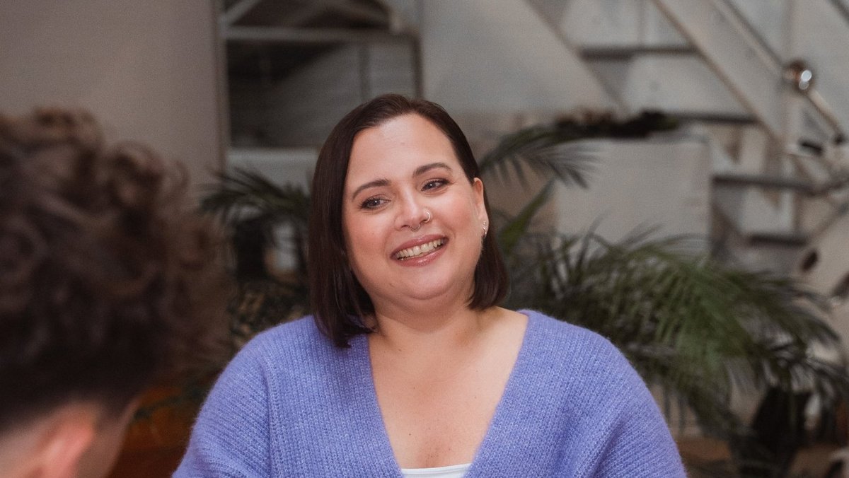 Жінка сидить у приміщенні та усміхається під час розмови.