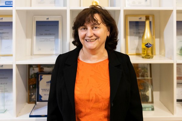 Жінка стоїть у діловому одязі та посміхається.