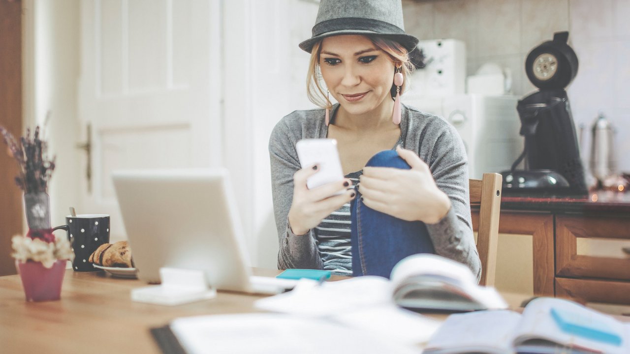 Жінка сидить за столом і користується ноутбуком та смартфоном