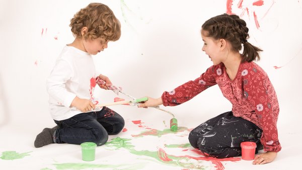 Двоє дітей сидять на підлозі та малюють разом.