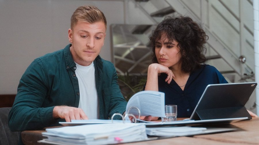 Двоє людей сидять за столом з документами та ноутбуком