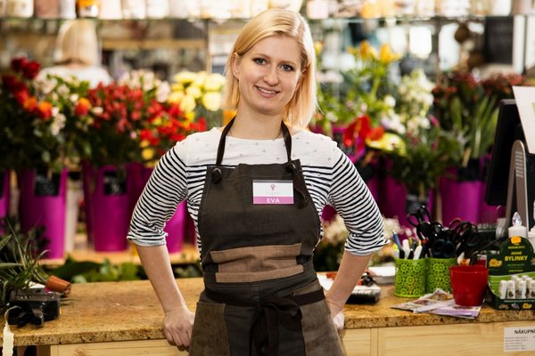 Жінка стоїть за прилавком з квітами та посміхається.