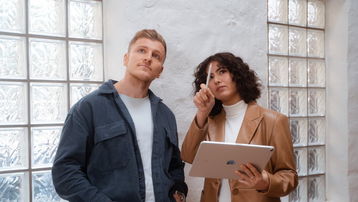 Чоловік і жінка стоять у приміщенні та дивляться на планшет.